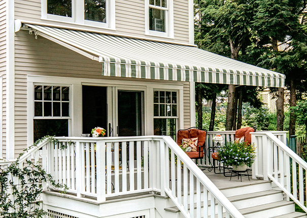 A white and green striped retractable awning covers a large back porch on a tan house.