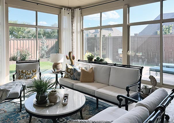 Black and white outdoor cushioned furniture surrounds a round coffee table in a glass sunroom patio enclosure.
