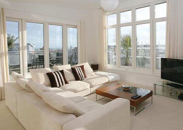 A white traditional sunroom with expansive windows, floor-length drapes and large white sectional sofa, coffee table and TV.
